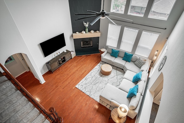 living room with a high ceiling, hardwood / wood-style floors, a tile fireplace, and ceiling fan