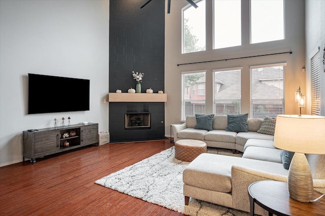 living room featuring a tiled fireplace, plenty of natural light, hardwood / wood-style flooring, and a high ceiling