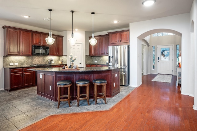 kitchen featuring a kitchen island, appliances with stainless steel finishes, decorative light fixtures, decorative backsplash, and dark wood-type flooring