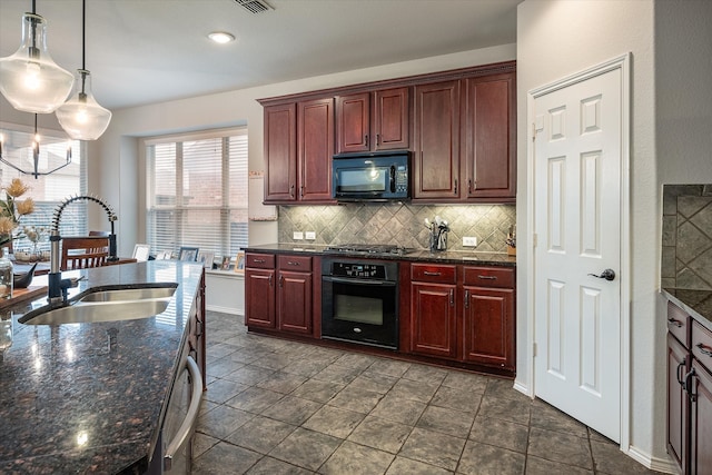 kitchen with dark stone counters, hanging light fixtures, black appliances, sink, and backsplash