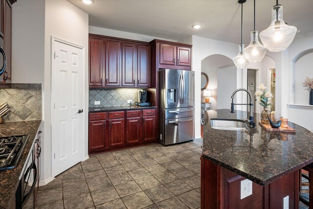 kitchen with appliances with stainless steel finishes, hanging light fixtures, sink, decorative backsplash, and an island with sink