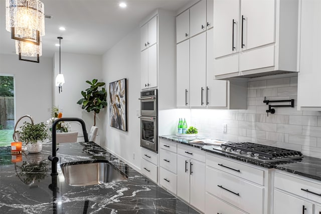 kitchen with sink, stainless steel appliances, backsplash, dark stone counters, and white cabinets