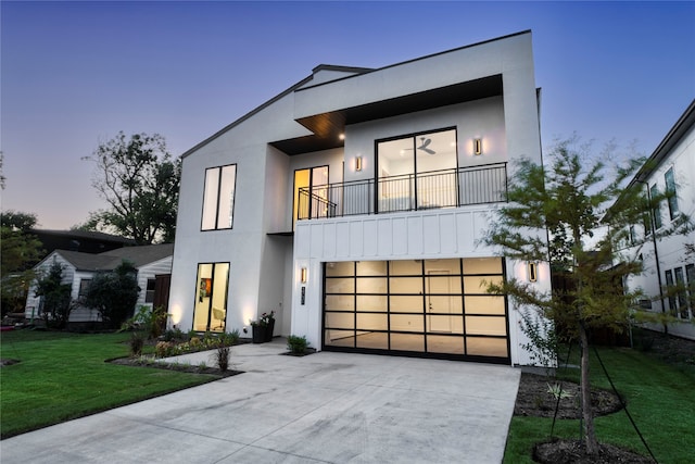 contemporary home with a balcony, a garage, and a lawn