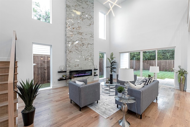 living room with a fireplace, plenty of natural light, a towering ceiling, and light hardwood / wood-style flooring