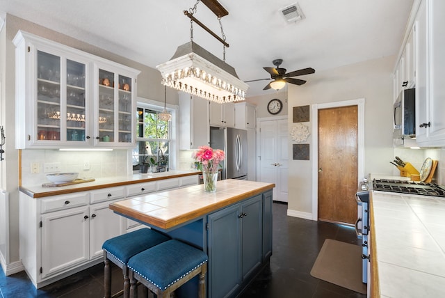 kitchen with tile counters, stainless steel appliances, white cabinets, backsplash, and decorative light fixtures