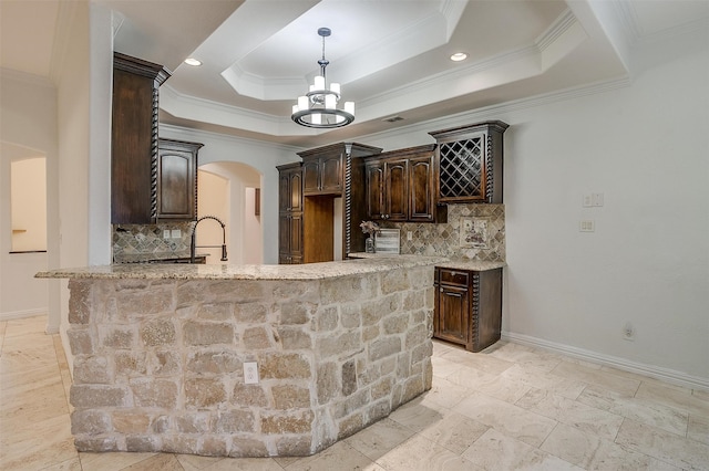 kitchen with kitchen peninsula, a tray ceiling, dark brown cabinets, crown molding, and light stone counters