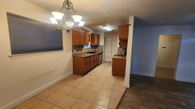 kitchen with sink, tasteful backsplash, hanging light fixtures, dishwasher, and a notable chandelier