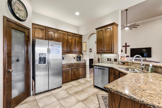 kitchen featuring sink, light stone counters, appliances with stainless steel finishes, decorative light fixtures, and vaulted ceiling