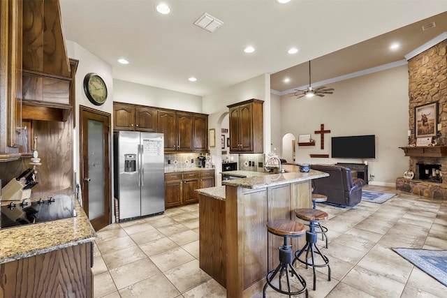 kitchen with stainless steel fridge, black electric stovetop, a breakfast bar area, kitchen peninsula, and ceiling fan