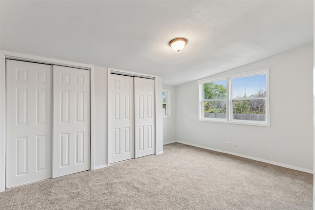 unfurnished bedroom featuring multiple closets, a textured ceiling, vaulted ceiling, and carpet floors