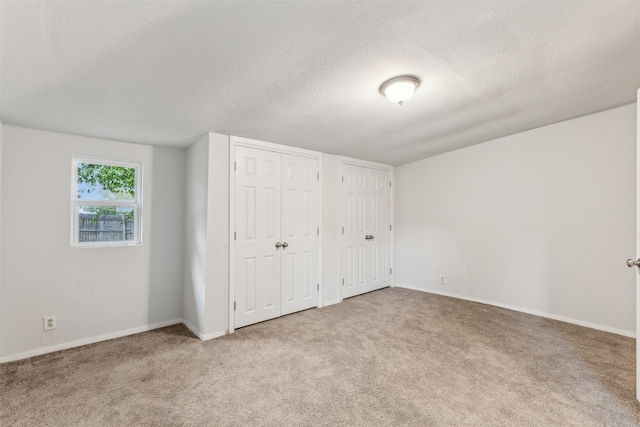 unfurnished bedroom with carpet, a textured ceiling, and two closets