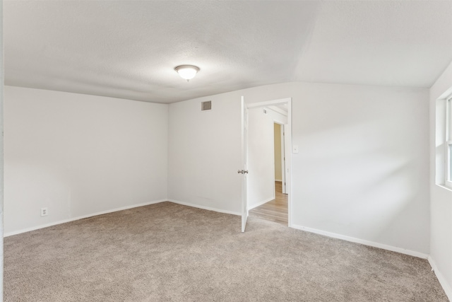 carpeted spare room with a textured ceiling and vaulted ceiling