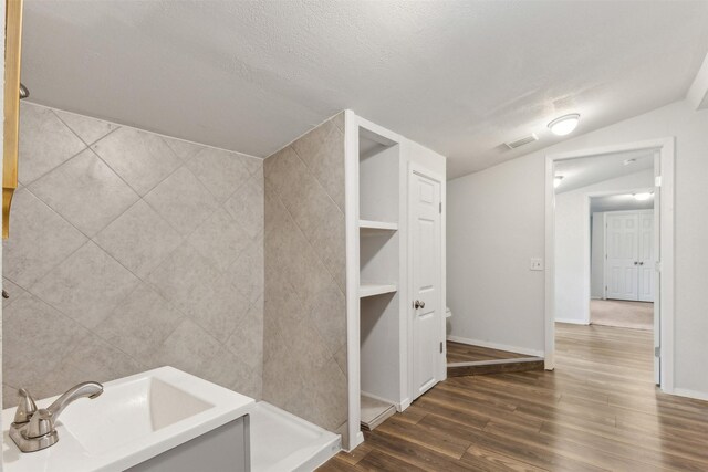 bathroom with tile walls, a textured ceiling, wood-type flooring, built in features, and vaulted ceiling