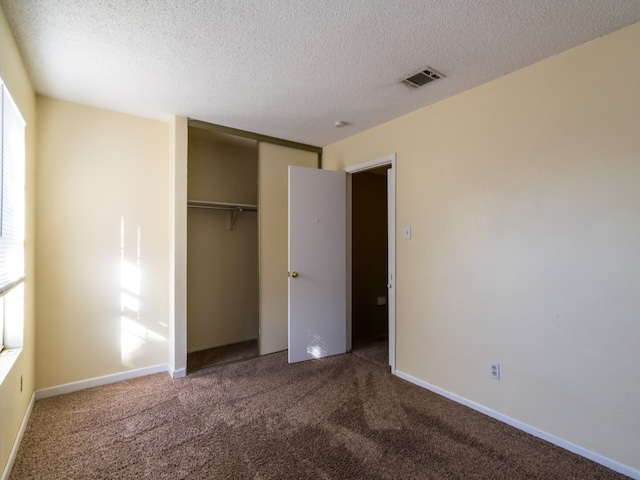 unfurnished bedroom featuring dark colored carpet, a textured ceiling, and a closet