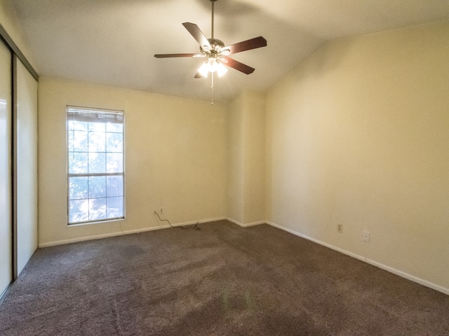 empty room featuring lofted ceiling, ceiling fan, and dark carpet