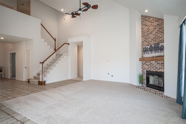 unfurnished living room with ceiling fan, light colored carpet, a fireplace, and a high ceiling