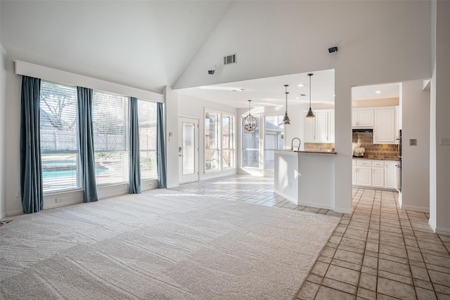 unfurnished living room with high vaulted ceiling, light carpet, and a notable chandelier