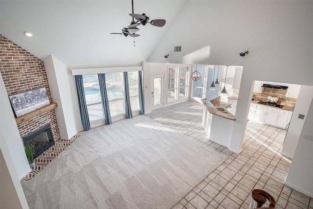 carpeted living room with a brick fireplace, high vaulted ceiling, and ceiling fan