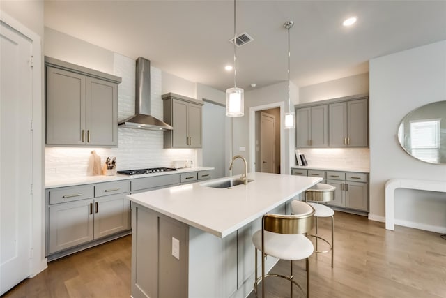 kitchen featuring hanging light fixtures, light hardwood / wood-style floors, wall chimney exhaust hood, and stainless steel gas cooktop