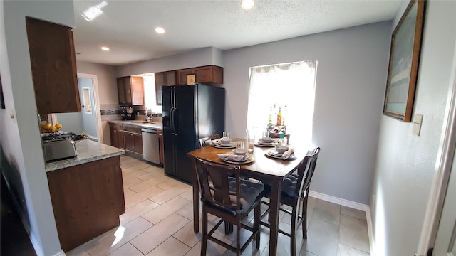 kitchen with dishwasher, black fridge, a healthy amount of sunlight, and light stone counters