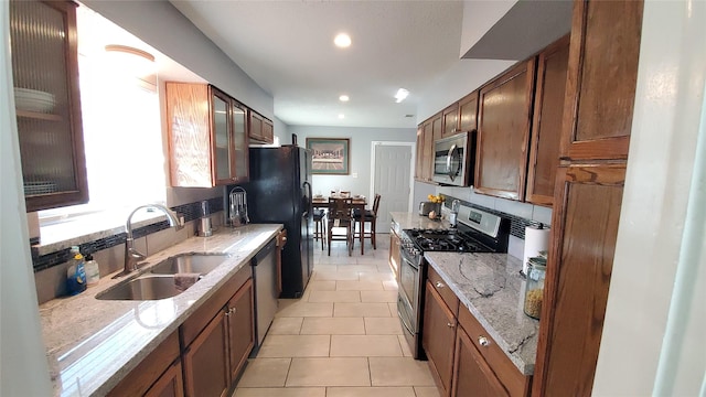 kitchen with appliances with stainless steel finishes, light tile patterned floors, light stone counters, and sink