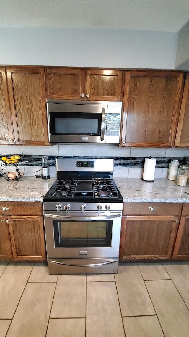 kitchen with stainless steel appliances, light stone countertops, and backsplash