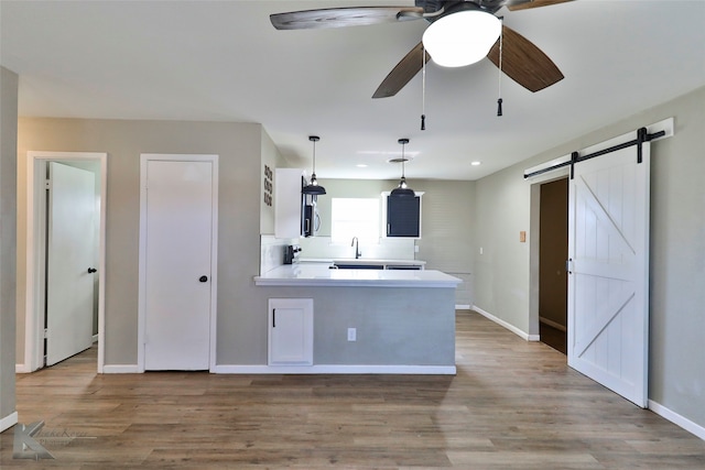 kitchen featuring kitchen peninsula, ceiling fan, hanging light fixtures, a barn door, and light wood-type flooring