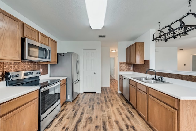 kitchen with sink, pendant lighting, light hardwood / wood-style floors, decorative backsplash, and appliances with stainless steel finishes