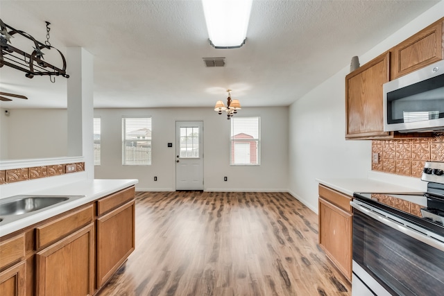 kitchen with backsplash, ceiling fan with notable chandelier, stainless steel appliances, sink, and light hardwood / wood-style floors