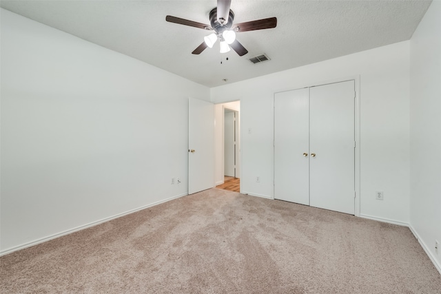 unfurnished bedroom featuring light carpet, a textured ceiling, a closet, and ceiling fan