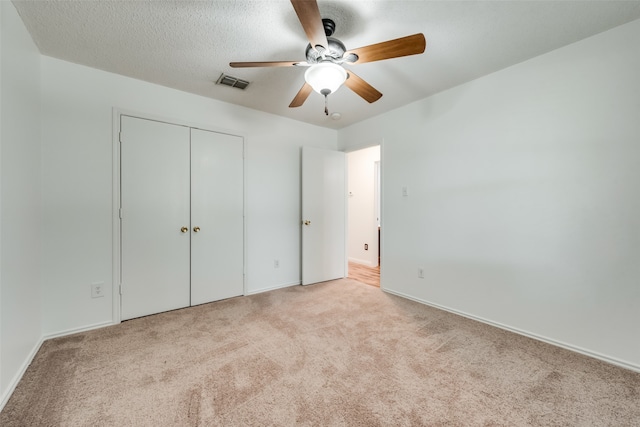 unfurnished bedroom with ceiling fan, light colored carpet, a textured ceiling, and a closet