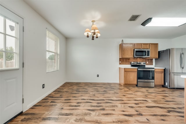 kitchen featuring hardwood / wood-style flooring, backsplash, appliances with stainless steel finishes, and a chandelier