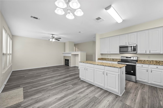 kitchen featuring white cabinetry, appliances with stainless steel finishes, hanging light fixtures, and a tiled fireplace