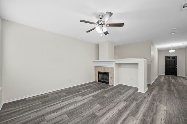 unfurnished living room featuring dark hardwood / wood-style flooring, a tiled fireplace, and ceiling fan