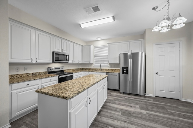 kitchen featuring stainless steel appliances, a center island, white cabinets, hanging light fixtures, and light hardwood / wood-style flooring