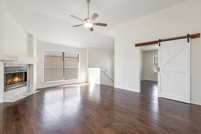 unfurnished living room with a textured ceiling, a barn door, ceiling fan, and dark wood-type flooring