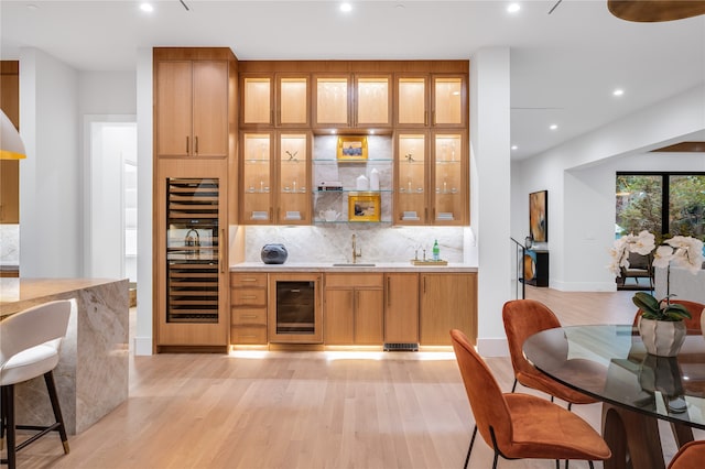 bar featuring beverage cooler, decorative backsplash, and light hardwood / wood-style flooring