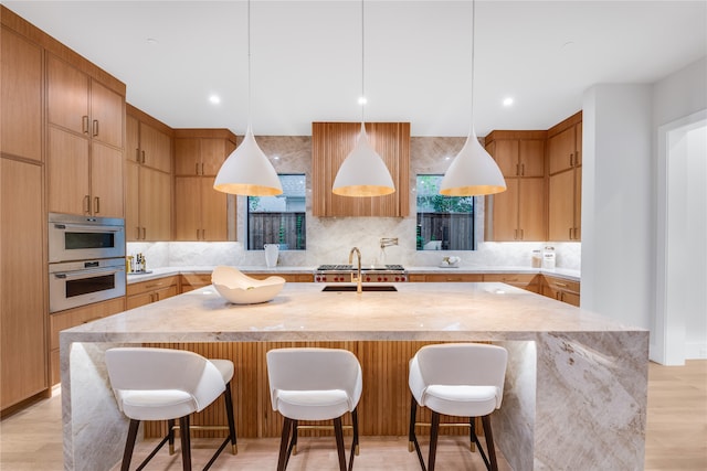 kitchen with light hardwood / wood-style floors, a center island with sink, a breakfast bar, stainless steel double oven, and pendant lighting