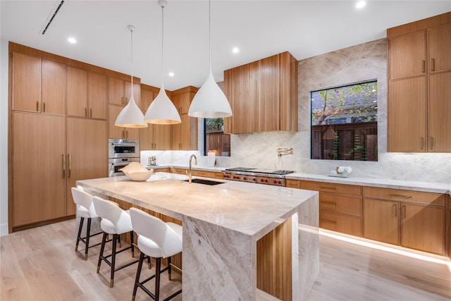 kitchen featuring a center island with sink, sink, a breakfast bar, light wood-type flooring, and pendant lighting