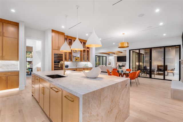 kitchen with a spacious island, backsplash, decorative light fixtures, sink, and light hardwood / wood-style flooring