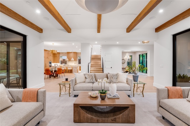 living room featuring light hardwood / wood-style flooring, beamed ceiling, and an inviting chandelier