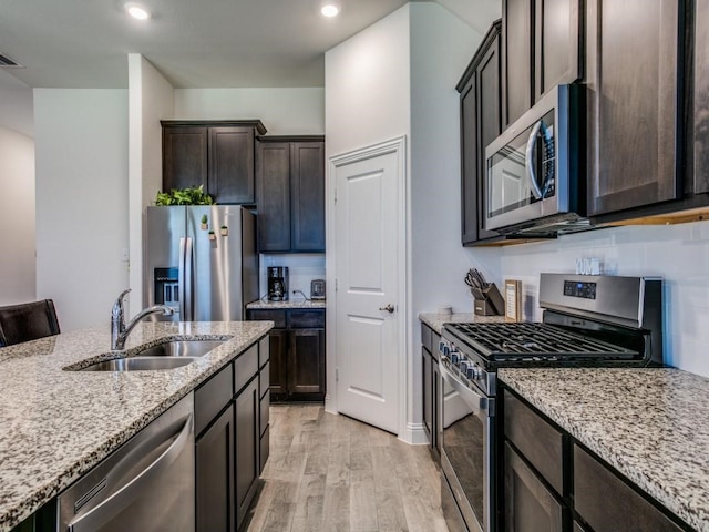 kitchen with light stone counters, stainless steel appliances, dark brown cabinets, sink, and light hardwood / wood-style flooring