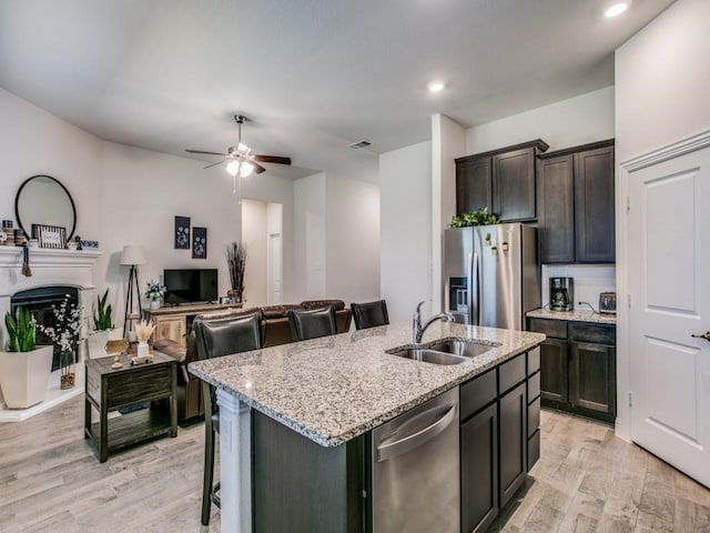 kitchen with a center island with sink, stainless steel appliances, sink, a kitchen breakfast bar, and light hardwood / wood-style flooring