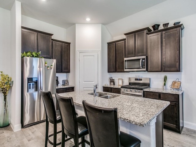 kitchen with stainless steel appliances, dark brown cabinetry, sink, an island with sink, and light wood-type flooring