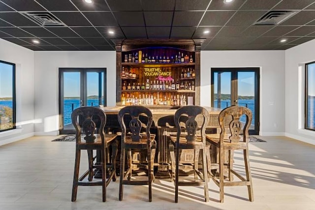 bar with a water view, french doors, and light hardwood / wood-style flooring