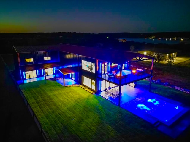 back house at dusk featuring a lawn and a patio area