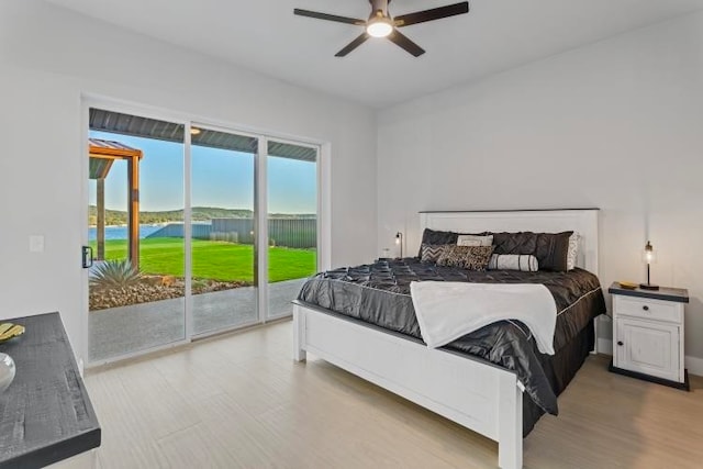 bedroom with access to outside, ceiling fan, a water view, and hardwood / wood-style flooring