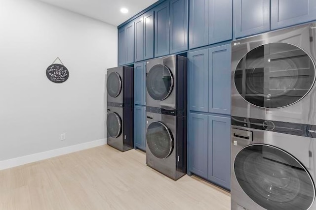 laundry room with stacked washer and dryer, light wood-type flooring, and cabinets