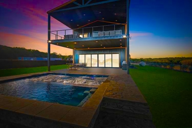 back house at dusk featuring a balcony, a yard, and a patio area