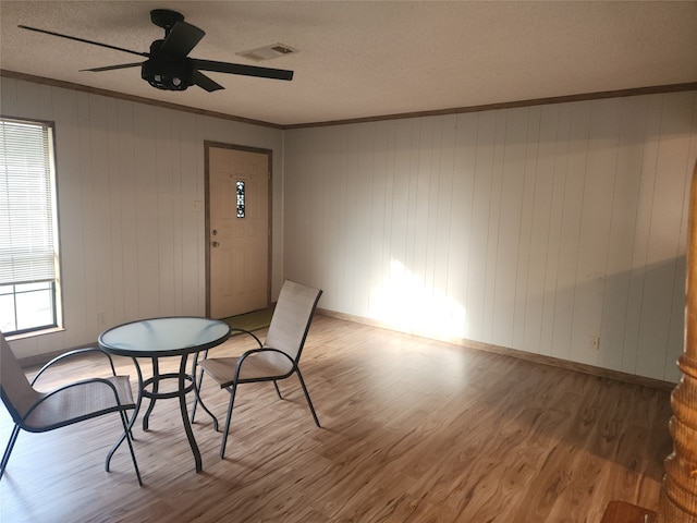 dining room with ceiling fan, wood-type flooring, a textured ceiling, wooden walls, and ornamental molding